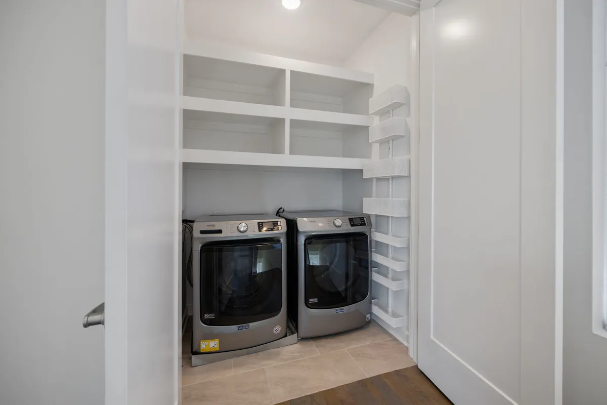 A bright, functional laundry room featuring washing machines, shelves for organization, and ample space for managing laundry tasks. The area is well-lit and designed for efficiency, making it easy for guests to maintain fresh clothing during their stay.