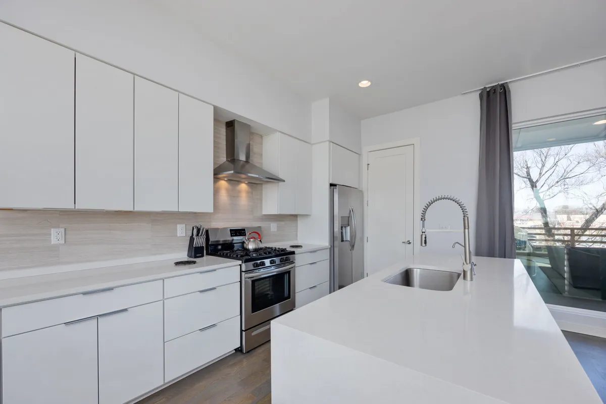 A contemporary kitchen featuring a large kitchen island, gleaming stainless steel appliances, and a wide window that brings in ample daylight. The setup encourages socializing while cooking or dining, with plenty of space for guests to join the conversation.