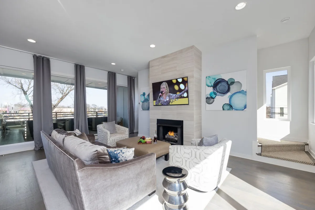 A contemporary living room featuring plush sofas arranged around a glowing fireplace, with a large smart TV mounted above. The space is accented by stylish artwork and designer decor, creating a cozy yet elegant atmosphere ideal for both relaxation and lively gatherings.