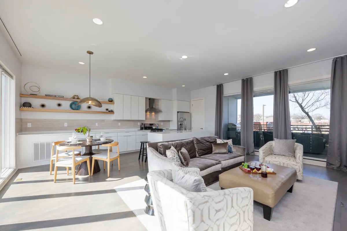 An open-plan space that seamlessly connects a sectional sofa, a spacious dining area, and large windows bathing the area in natural light. The scene feels airy and modern, perfect for gatherings, family meals, and relaxed conversation.