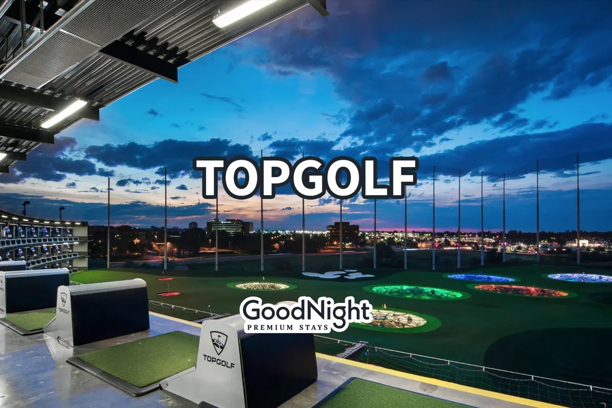 Dynamic exterior shot of a Topgolf venue with bays lit up and the Nashville skyline in the distance. LED targets on the field hint at a lively, social golfing experience beyond traditional courses.